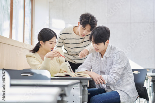 Three young male and female college students models sitting or standing at desks in a university classroom in South Korea, Asia, talking or having a discussion