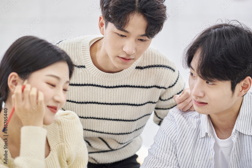 Three young male and female college students models sitting or standing at desks in a university classroom in South Korea, Asia, talking or having a discussion Three young male and female college students models sitting or standing at desks in a university classroom in South Korea, Asia, talking or having a discussion