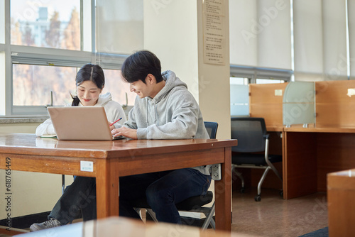 Three young male and female college students models sitting or standing at desks in a university classroom in South Korea, Asia, talking or having a discussion