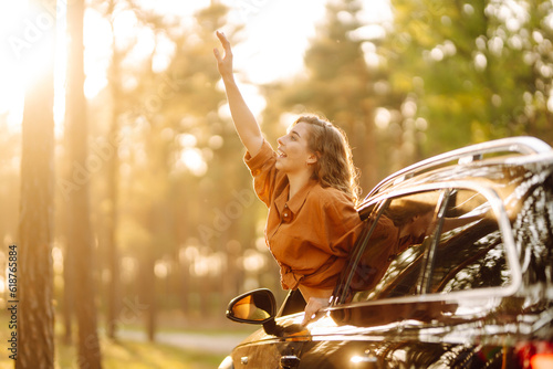 Beautiful traveler woman is resting and enjoying the sunset in the car. Happy woman on a summer trip, travels leaning out of the car window. Active lifestyle, tourism. Travel concept. photo