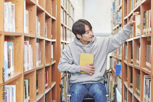 Asia South Korea university library bookcase in a wheelchair looking for a book on the shelf, physically handicapped young disabled male college student model