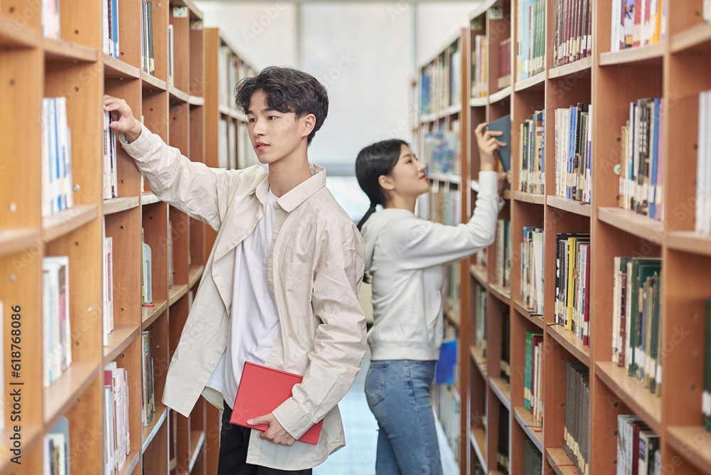 Two young male and female college students looking for and looking at books on the shelves of a university library in South Korea, Asia Two young male and female college students looking for and looking at books on the shelves of a university library in South Korea, Asia
