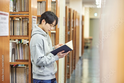 A young man attending college is browsing and reading books on the shelves with different expressions in his university library in South Korea, Asia.