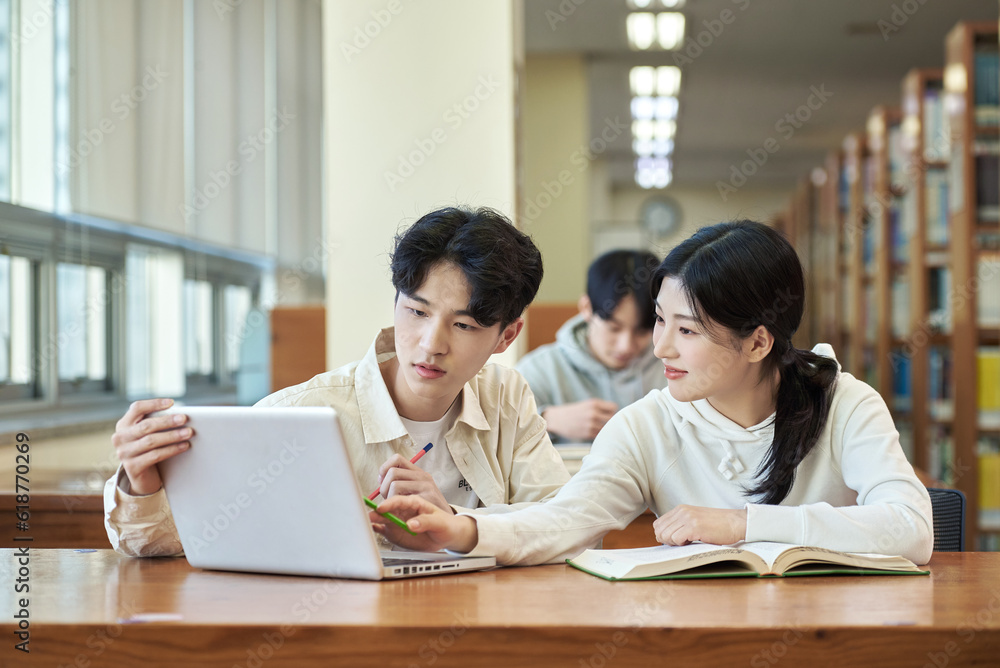 Two young college student man and woman couple model and solo male model looking at laptop and book together in library of Asian Korean university Two young college student man and woman couple model and solo male model looking at laptop and book together in library of Asian Korean university