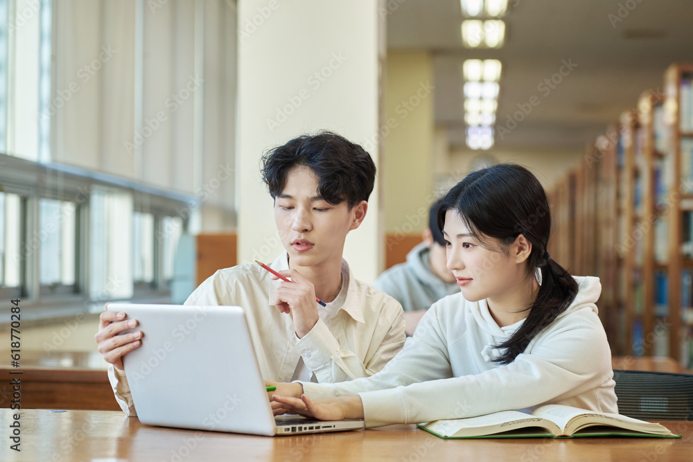 Two young college student man and woman couple model and solo male model looking at laptop and book together in library of Asian Korean university Two young college student man and woman couple model and solo male model looking at laptop and book together in library of Asian Korean university