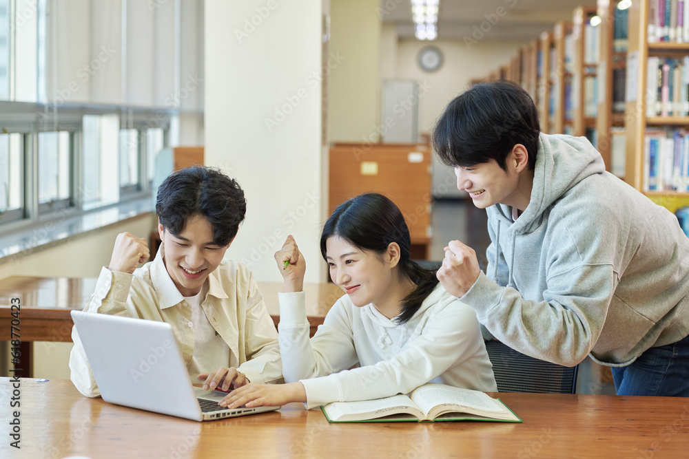 Two young college student man and woman couple model and solo male model looking at laptop and book together in library of Asian Korean university Two young college student man and woman couple model and solo male model looking at laptop and book together in library of Asian Korean university