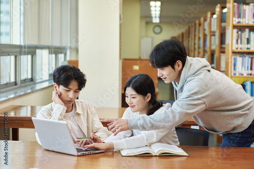 Two young college student man and woman couple model and solo male model looking at laptop and book together in library of Asian Korean university