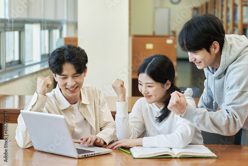 Two young college student man and woman couple model and solo male model looking at laptop and book together in library of Asian Korean university