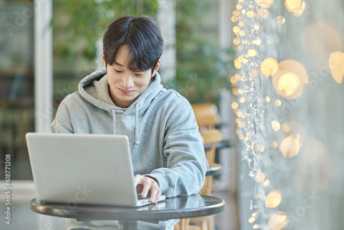 Young male college student model sitting at a cafe table in Asian Korea, listening to a lecture, doing homework or working on a laptop with blurred lights in the background