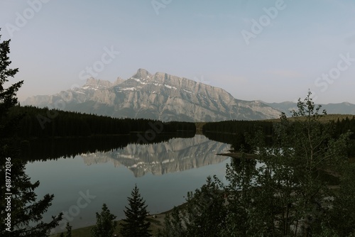 Stunning rugged mountain surrounded by lush trees and a tranquil lake in the foreground