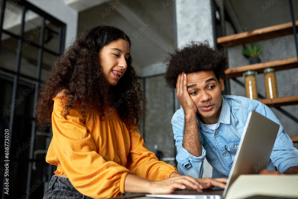 Side view of cute young enthusiastic black female using laptop, chatting in social media online or playing video game, sticking tongue while her african american boyfriend looking at screen with shock Side view of cute young enthusiastic black female using laptop, chatting in social media online or playing video game, sticking tongue while her african american boyfriend looking at screen with shock