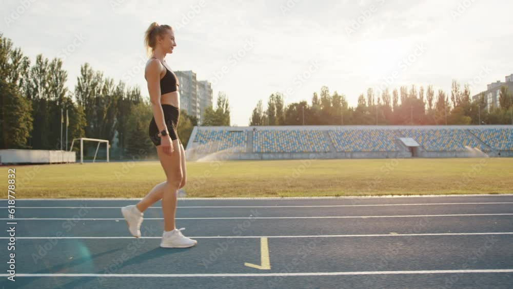 Profile shot of sexy athletic young blonde walking along running track outdoors. Woman relaxes after running in the stadium on a sunny morning. Sprint. High quality 4k footage Profile shot of sexy athletic young blonde walking along running track outdoors. Woman relaxes after running in the stadium on a sunny morning. Sprint. High quality 4k footage