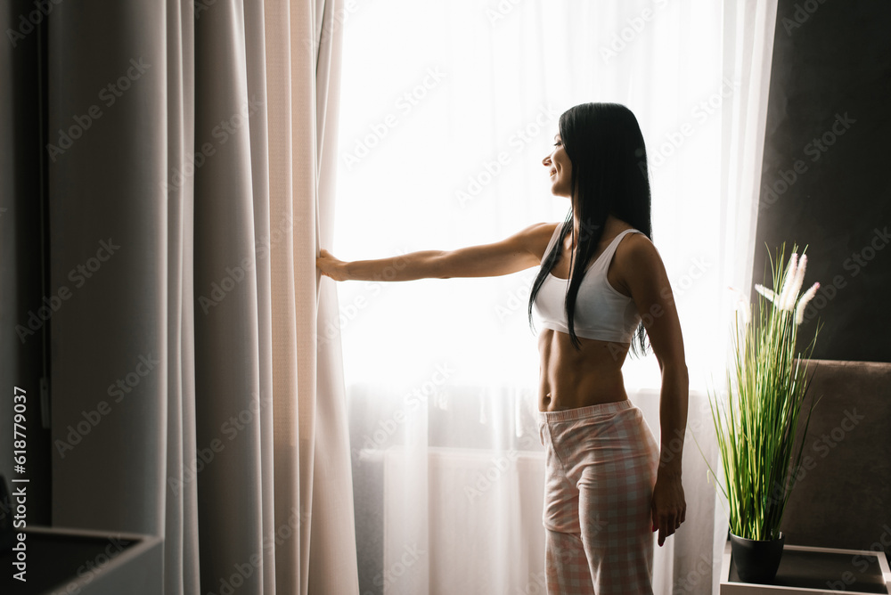 Woman stands at the bedroom window in the morning