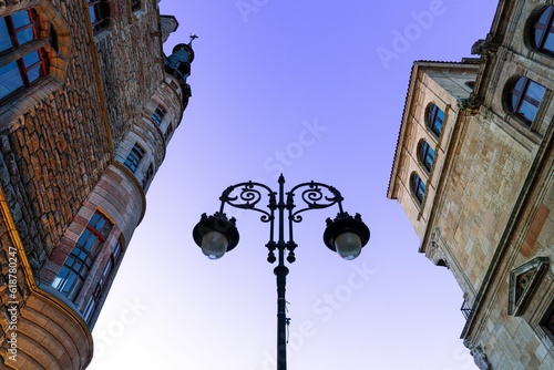 Fototapeta Naklejka Na Ścianę i Meble -  Low angle of a street lamp between old buildings at sunset in Leon, France