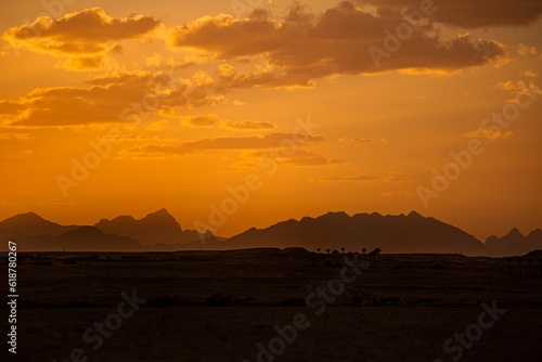 Orange sky with silhouetted mountains in the distance in a desert in Africa.
