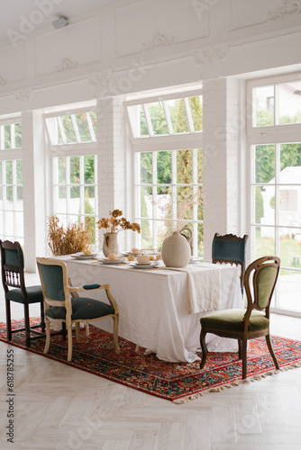 Table set for Thanksgiving with vintage chairs of different shapes and colors in a bright living room with French windows