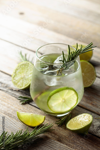 Gin tonic with ice, rosemary, and lime slices on an old wooden table.