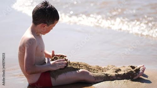 Little boy Kid sitting close to a Sea Shore, playing with Sand