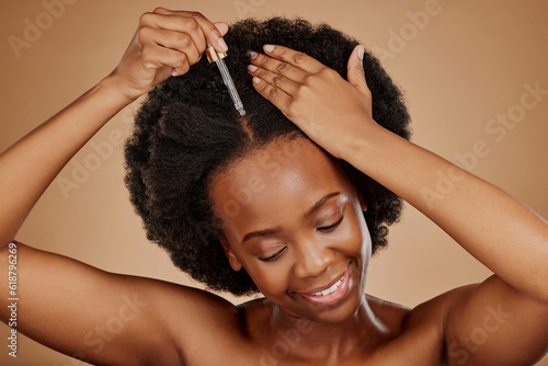 Oil serum, hair care or black woman with afro in studio on brown background for a healthy scalp. Smile, pipette or natural African girl at hairdresser salon for hairstyle treatment or beauty makeover