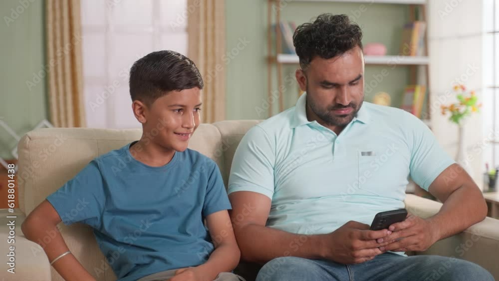 Happy smiling indian son giving greeting card to father by embracing while sitting on sofa at home - concept of family relationship, affectionate and father's day Happy smiling indian son giving greeting card to father by embracing while sitting on sofa at home - concept of family relationship, affectionate and father's day
