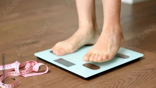 White floor scales and women's feet standing on them. A tailor's centimeter or measuring tape lying nearby to measure body changes. The concept of a healthy lifestyle and body weight tracking