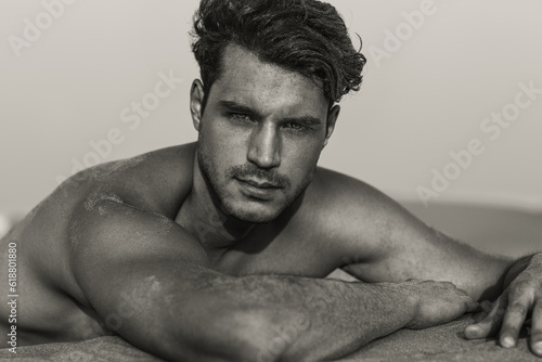 Sexy portrait of a handsome topless male model with beautiful eyes lying on the sand. 