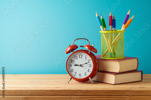 Back to school background with pencils, books and alarm clock on wooden table over blue background