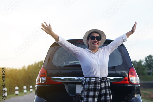 Happy Asian woman traveller wears hat, white shirt and sunglasses, raise hands up to sky at the back of car, feels free. Concept, relax time. Vacation  trip by private vehicle. Give time for yourself. #618824047