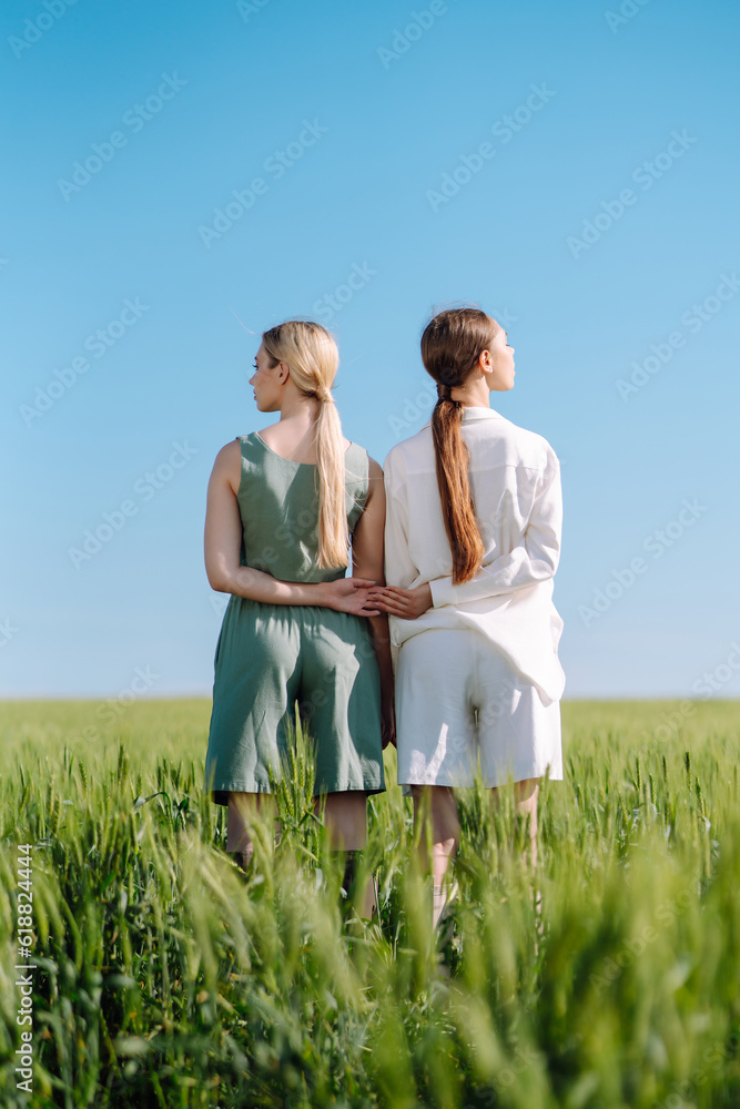 Two stylish women posing in a green field. Beautiful girlfriends in stylish clothes walk along the green field. Fashion, style concept. Summer landscape. Two stylish women posing in a green field. Beautiful girlfriends in stylish clothes walk along the green field. Fashion, style concept. Summer landscape.