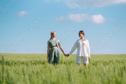 Two stylish women posing in a green field. Beautiful girlfriends in stylish clothes walk along the green field. Fashion, style concept. Summer landscape.