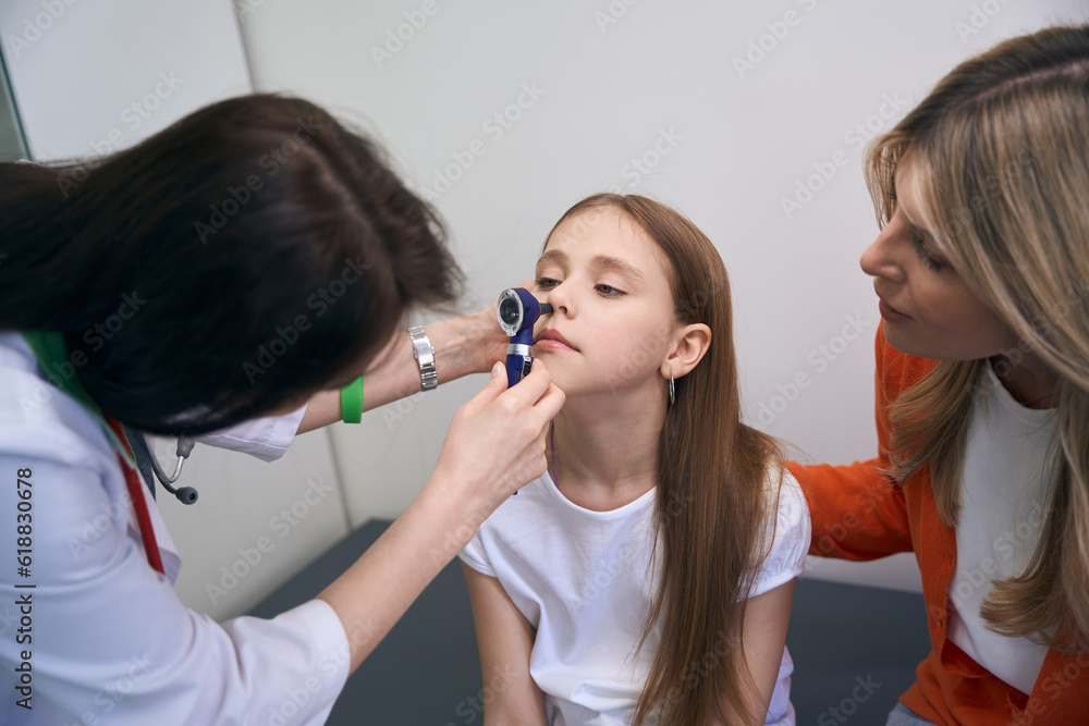 Caring laryngologist checking girl nose using specialized tool Caring laryngologist checking girl nose using specialized tool