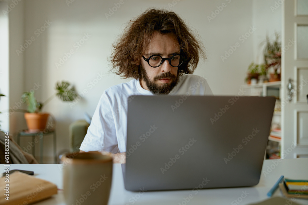Thoughtful man freelancer sitting at desk and working at laptop in home office. Remote work Thoughtful man freelancer sitting at desk and working at laptop in home office. Remote work