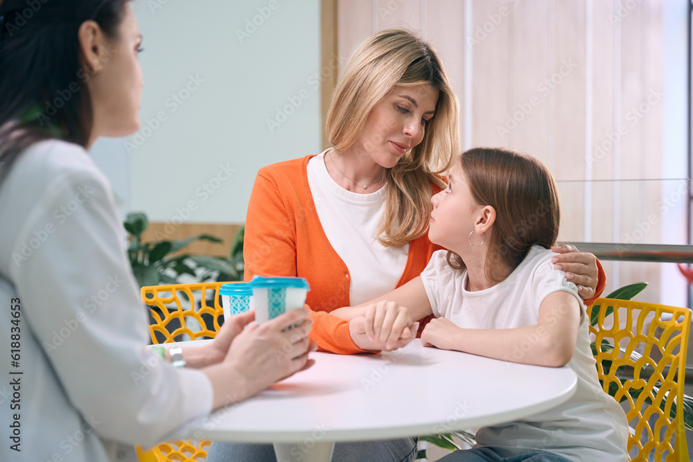 Caring mother calming down little daughter talking to pediatrician Caring mother calming down little daughter talking to pediatrician