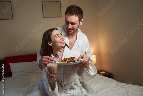 Romantic guy treating his wife with pancakes in hotel room