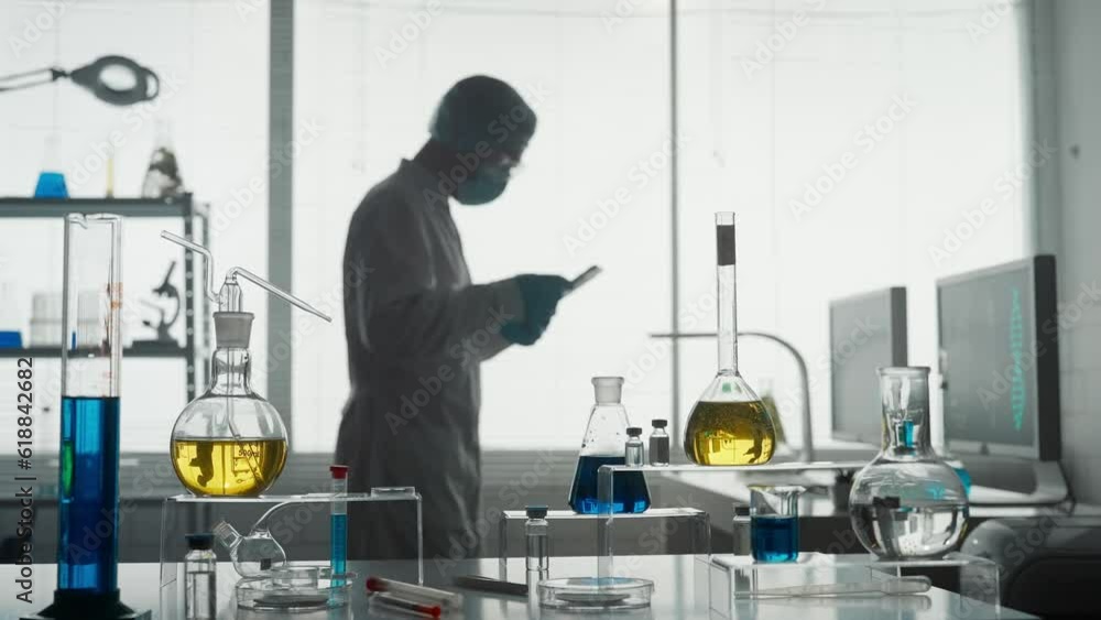 Laboratory of modern medical research. A male researcher uses a tablet in a laboratory. A man analyzes a green liquid in a flask. Blurred background. Laboratory of modern medical research. A male researcher uses a tablet in a laboratory. A man analyzes a green liquid in a flask. Blurred background.