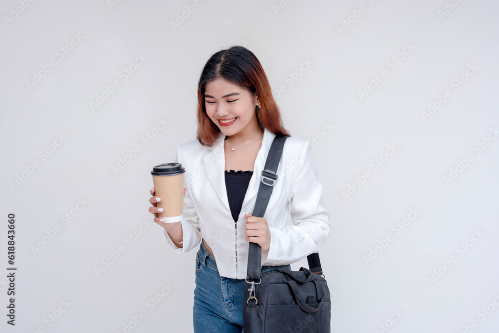 A smiling young woman with messenger bag looking at a disposable coffee cup she's holding. Isolated on a white background. A smiling young woman with messenger bag looking at a disposable coffee cup she's holding. Isolated on a white background.