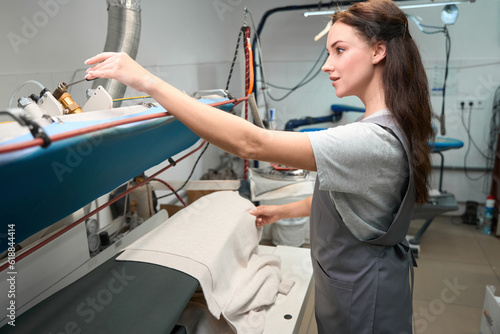 Skilled woman dry-cleaning service worker pressing clothes on special board