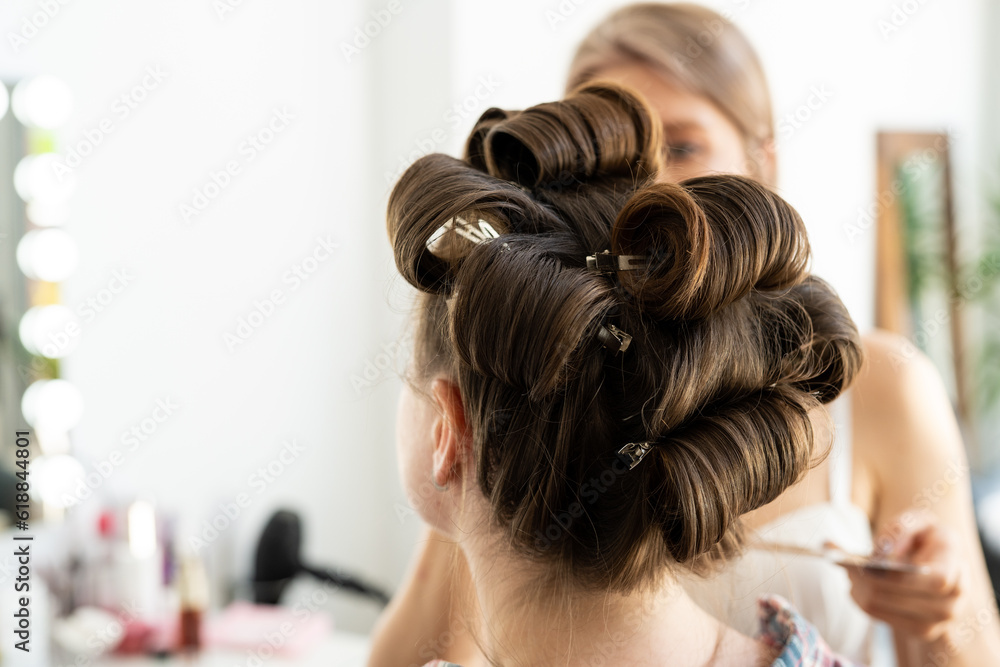 Fototapeta premium The hairdresser curls the model's hair. Curling iron for curling hair close-up.