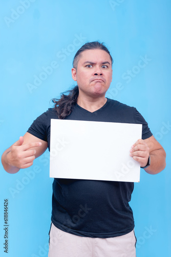Obraz na płótnie A biracial male with undercut and pursed lips angrily holding a blank placard while pointing at it with one hand