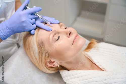 Smiling adult woman getting face injection in beauty salon