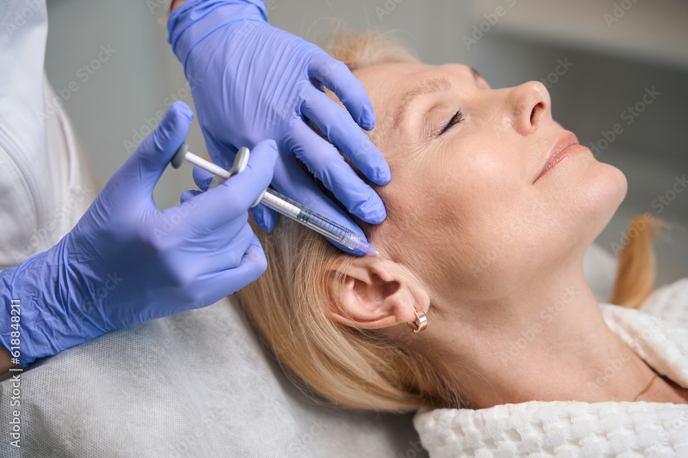 Adult woman getting temple injection in beauty salon Adult woman getting temple injection in beauty salon