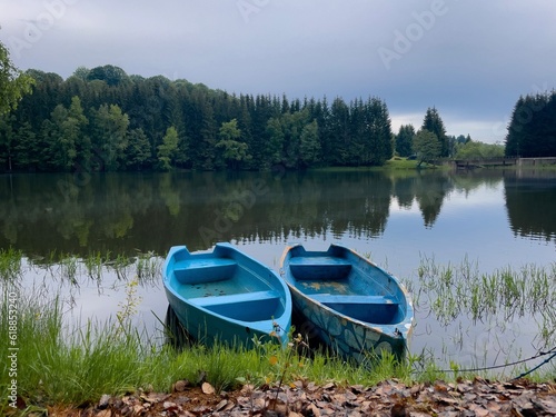 Two blue wooden boat on a lake surrounded by coniferous trees