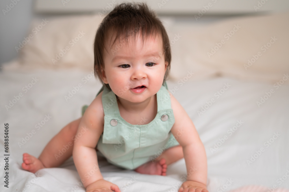 Mixed ethnicity Asian Caucasian 8 months baby girl - lifestyle home portrait of adorable and happy female child lying playful on bed exploring the surroundings curious