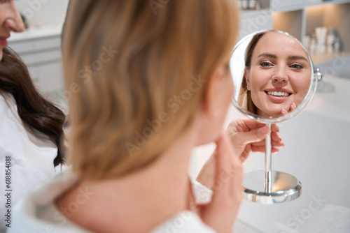 Happy female blonde looks inirror at consultation with esthetician