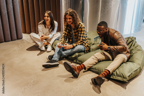 Wallpaper Mural Three multiracial colleagues taking a break from work. They are sitting on a lazy bags while playing electronic games. Having fun at work concept Torontodigital.ca