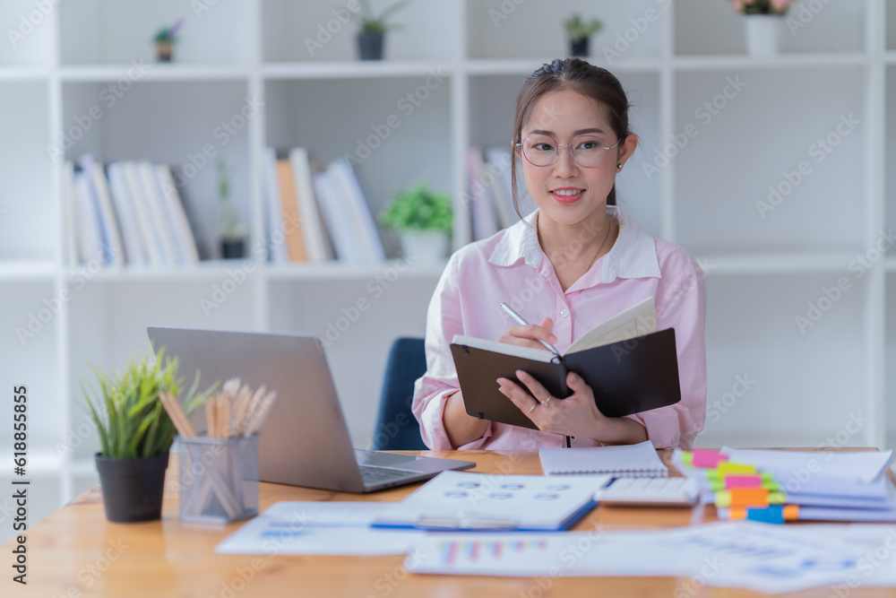 Sharing good business news. Attractive young businesswoman Used the laptop with document and smiling while sitting at her working place in office.
