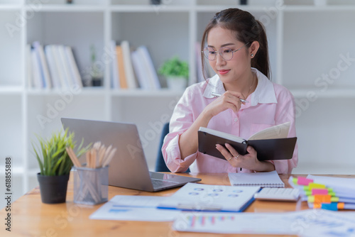 Sharing good business news. Attractive young businesswoman talking on the mobile phone and smiling while sitting at her working place in office and looking at laptop PC.