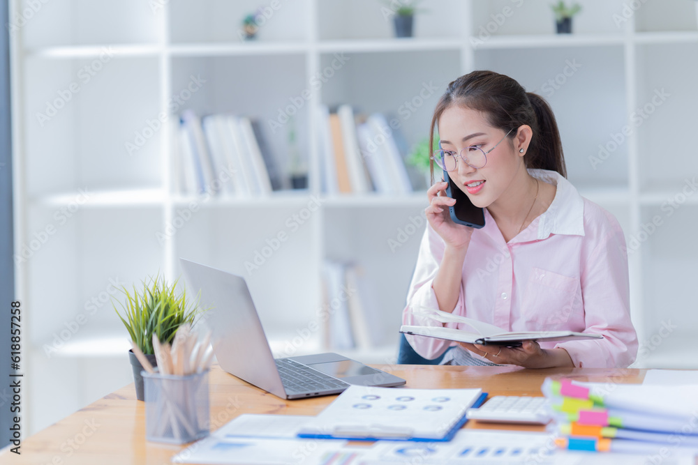 Image of smiling beautiful woman writing down notes while sitting at table in office Image of smiling beautiful woman writing down notes while sitting at table in office