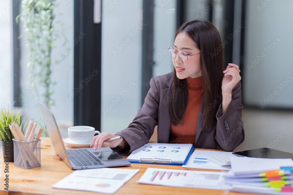 Sharing good business news. Attractive young businesswoman talking on the mobile phone and smiling while sitting at her working place in office and looking at laptop PC. Sharing good business news. Attractive young businesswoman talking on the mobile phone and smiling while sitting at her working place in office and looking at laptop PC.
