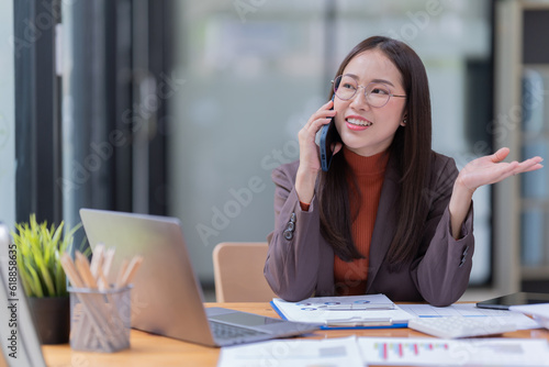 Smiling young Asian businesswoman sitting  with laptop computer on desk in the office.